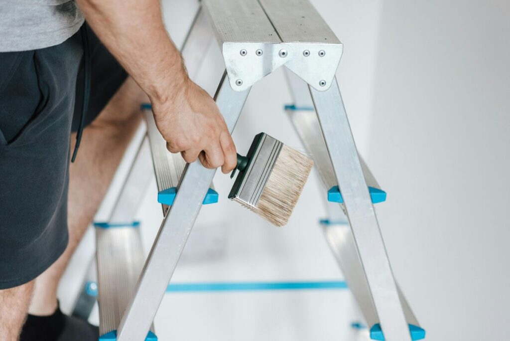 man holding paint brush on ladders
